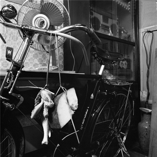 广州，居民家中的自行车和用稻草拴吊在车头的猪肉。自行车后面的桌上摆放着电风扇，柜子里放着录音机。